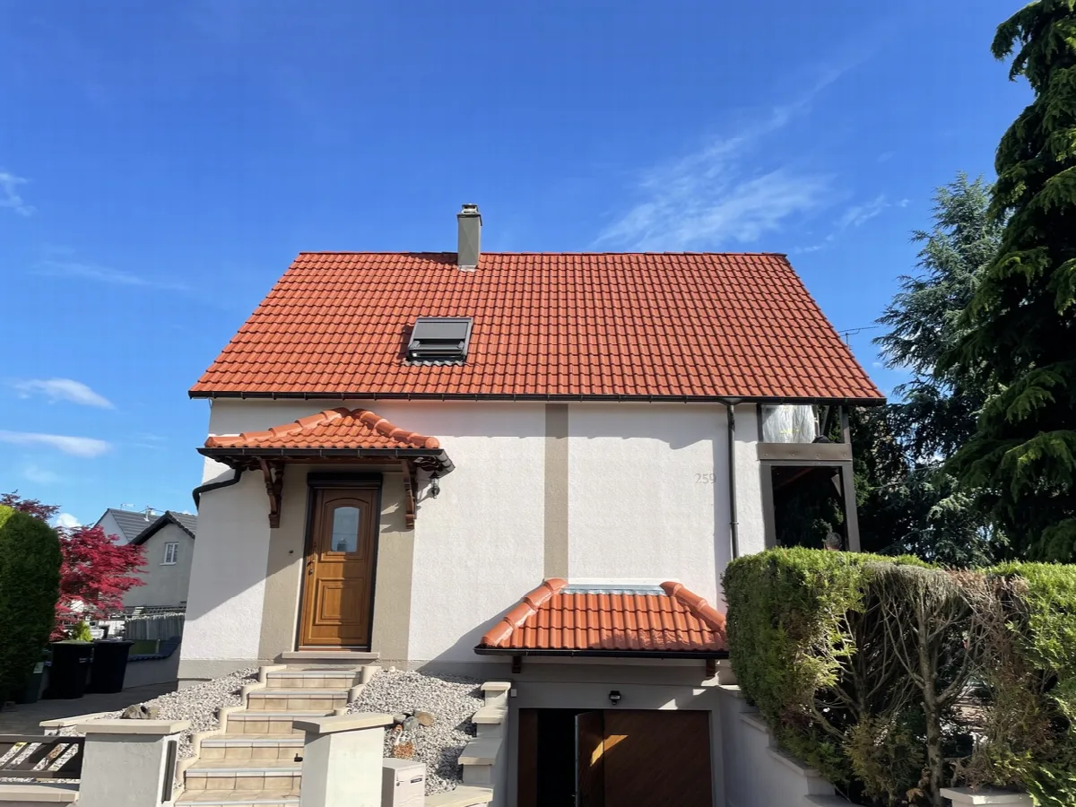 Maison blanche avec une couverture en tuiles rouges et une fenêtre de toit